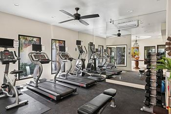 A spacious gym with treadmills, elliptical machines, and a ceiling fan.